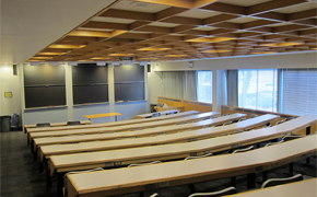 Photograph of a well-lit large lecture hall with gradually tiered seating and six chalkboards.