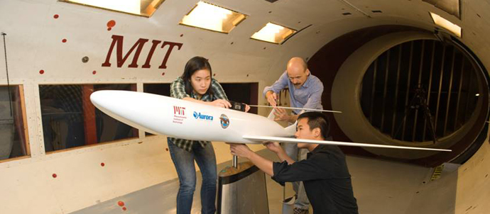 A woman and two men examine and take measurements of a model jet inside a wind tunnel.
