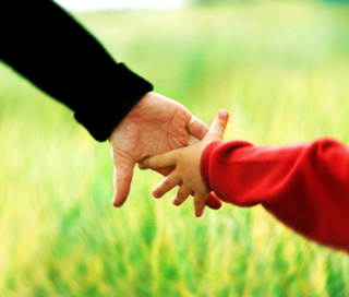 A woman in a black shirt holds hands with a child in a red shirt while walking in a field.