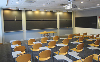 A classroom with four rows of chairs facing a small desk and chair positioned in front of a blackboard.