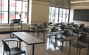 A well-lit, medium-sized room with open windows and four rows of desks and chairs.