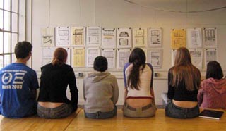Six students sit on the edge of a table reviewing each others work.