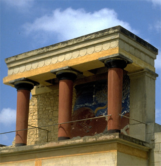 A photo of the Palace of Minos in Crete, specifically a balcony with three columns in front of a painted wall.