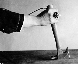 A black and white photo of a nail being pulled out of wood with a hammer.