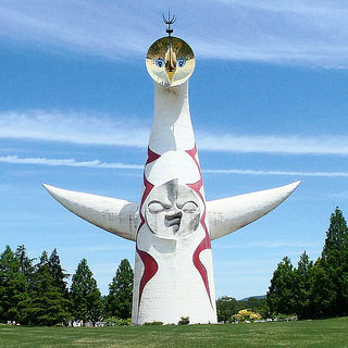 A photo of a cylindrical building with a face on it and outstretched arms.