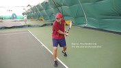 The right foot steps forward and across to the left, with the racket still behind the body, held in both hands.