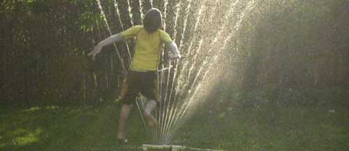 Child jumping through sprinkler, with sunlight.