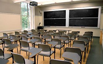 A photo of a classroom. There are individual desks facing two chalkboards at the front of the room.