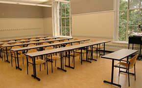 A classroom with chalkboards, several rows of flat tables for students, and a small table at the front for the instructor.