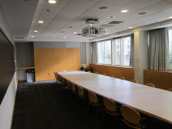 Image of a classroom with windows on the right, a chalkboard on the left,and a large center table in the middle.