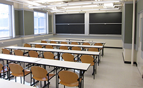 A photo of a classroom with sliding chalkboards, tables and chairs.