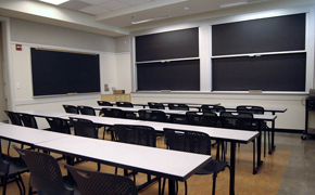 A functional classroom, with long tables, chairs, and lots of black boards.