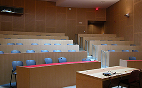 Photo of tiered tables and chairs with an instructors table at the front of the room. Modern wood paneling lines the walls.