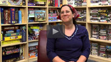 An image of instructor Sara Verrilli taken from an interview in which she is seated in front of large bookcases filled with various games.