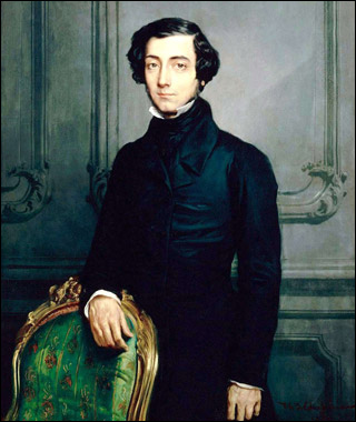 A slim smartly-dressed young man, with wavy black hair, stands behind an ornate chair.