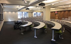 Five rows of tables with chairs facing a chalkboard. A window is on the side wall of the classroom.
