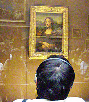 A photograph of the Mona Lisa taken at the Louvre. Crowds of people can be seen in the reflection of the glass that encases the painting.