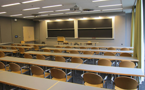 A photo of a classroom with five rows of tables and a blackboard at the front of the room.
