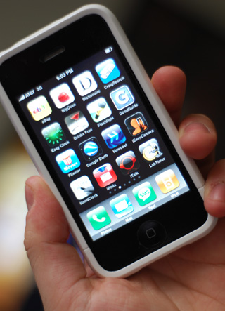 Photograph of a hand holding an Apple iPhone displaying a screen of icons for various apps.