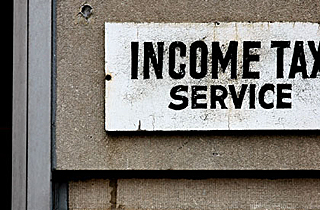 Photograph of a white sign with black print advertising income tax preparation.