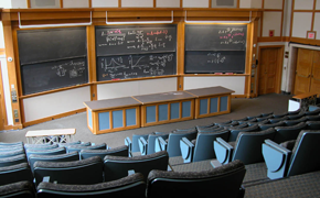 This classroom, which seats 135, has stadium-style rows of seats. At the front, there is a large table and six sliding chalkboards in a 3 wide by 2 high configuration.
