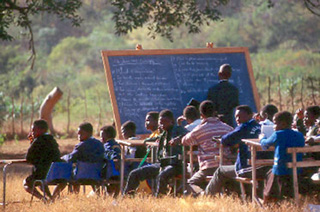 Students sit in a classroom in a grassy field.