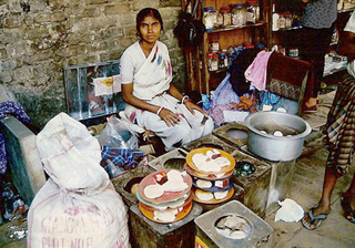 Photograph of a woman with stacks of food and medicinal supplies.