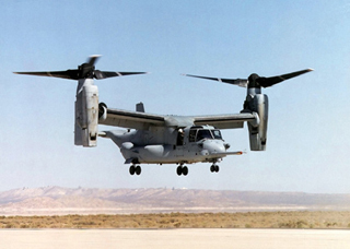 A photo of an CV-22 Osprey in rotorcraft mode, hovering above the ground.