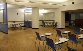 Large open room with small group areas separated by walls along the periphery. Tablet desks in the center of the room.