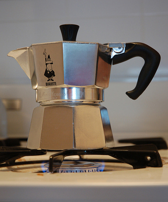 A shiny metal coffee pot sits on the burner of a stove.