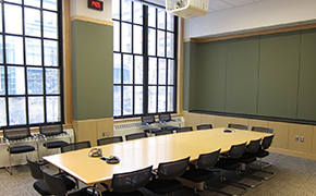 Classroom with two large windows and a long, rectangular seminar table surrounded by moveable chairs.