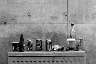 Black and white image of empty bottles on a metal lid with a concrete background.