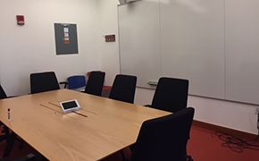 Small classroom with whiteboard lined walls and a single table in the center lined with chairs.