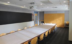 Small classroom with chalkboard lined walls and a single long table in the center lined with chairs.