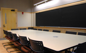 This photo shows a central table with chairs around all sides and a chalkboard on one wall.