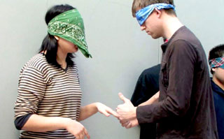 Two blindfolded students trying to communicate through hand signals.