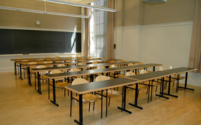 Photo of a classroom with long tables and chairs all facing multi-level chalkboards at the front of the room.