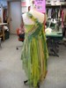 Seen from the back on a dress form, the dress has one strap coming across from the left shoulder to the bodice, which is made from silk strips in various shades of green, swept diagonally to the waist. The skirt falls raggedly past the knee, reaching the 