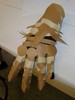 A more armor-like prototype, brown paper segments form overlapping wedges along the fingers and wrist to allow bending, while round pieces cover the knuckles, and triangular sections bristle on the back of the hand.