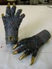 A pair of dark grey scaled monster claws, with long gold nails, scattered rhinestones in all colors, and a gold bracelet around one wrist.
