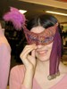 Gold mesh covered with purple chiffon forms the mask, with a meandering line of blue-green ribbon and sequins leading up to purple feathers at the upper right corner. A strip of fabric with coins attached at the bottom dangles from the left corner.