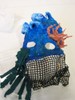 The bottom half of the mask is black Variform, with small shells attached. The top half is sculpted into blue waves along the hairline, and twisted orange coral on the left temple. Green fabric seaweed dangles from the right cheek.