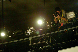 A photographer perched on a catwalk above a stage.