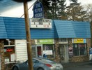 An facade of an urban convenience store called The Super Store. On the sign, Lucky and Olympia, with a few letters that do not form words, followed by $12.99