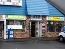 A close up of the front of an urban convenience store. Signs for beer, an ATM, coffee, and lottery cover the windows and door.
