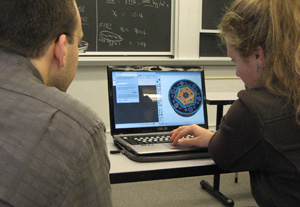 Dr. Short and a girl sit side by side working on a computer with the image of a colorful structure up on the screen.