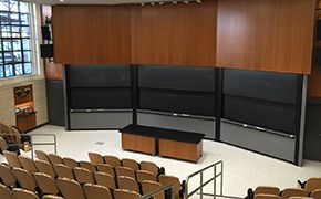 Tiered lecture seats facing three sets of sliding chalkboards. A large window on the left wall.