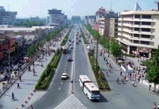 A photograph of a street in China.  The street is lined with pedestrians.
