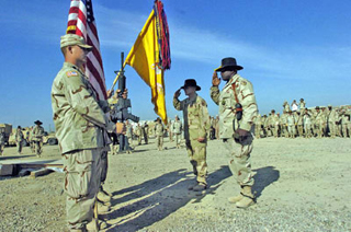 Assembled soldiers salute a flag in a desert setting.