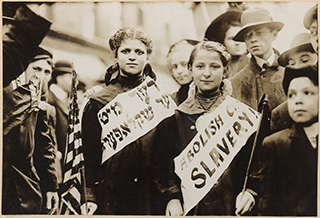 A photo from 1909 of two girls wearing banners that read "ABOLISH CHILD SLAVERY!" in English and Yiddish.